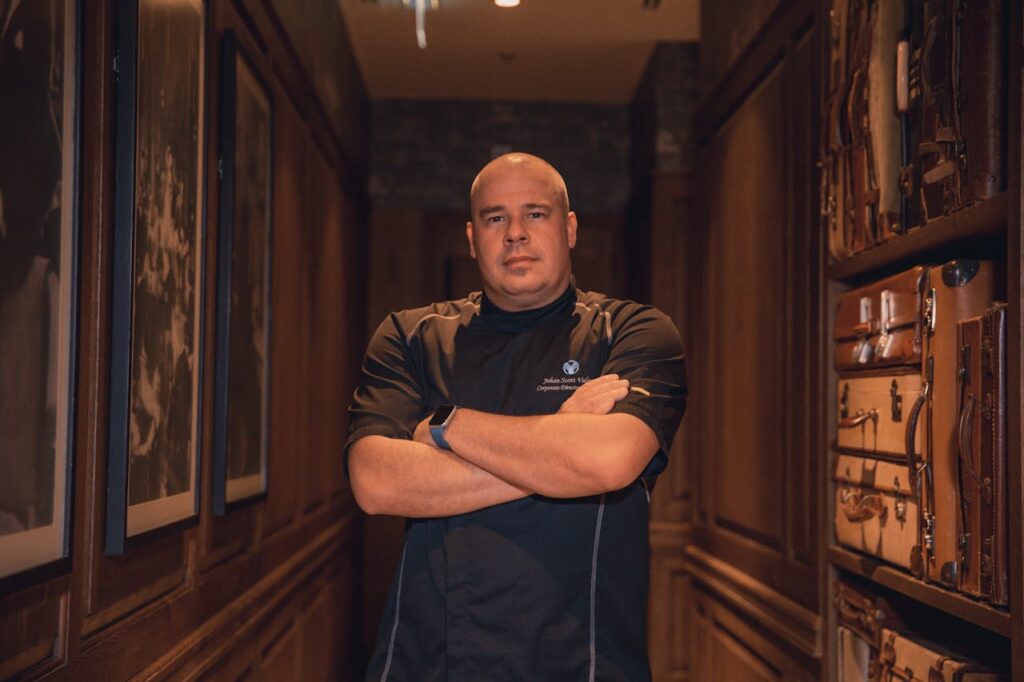 Mastering the First Impression: Your intriguing post title goes here Bald chef standing confidently indoors, arms crossed, in a stylish hallway.